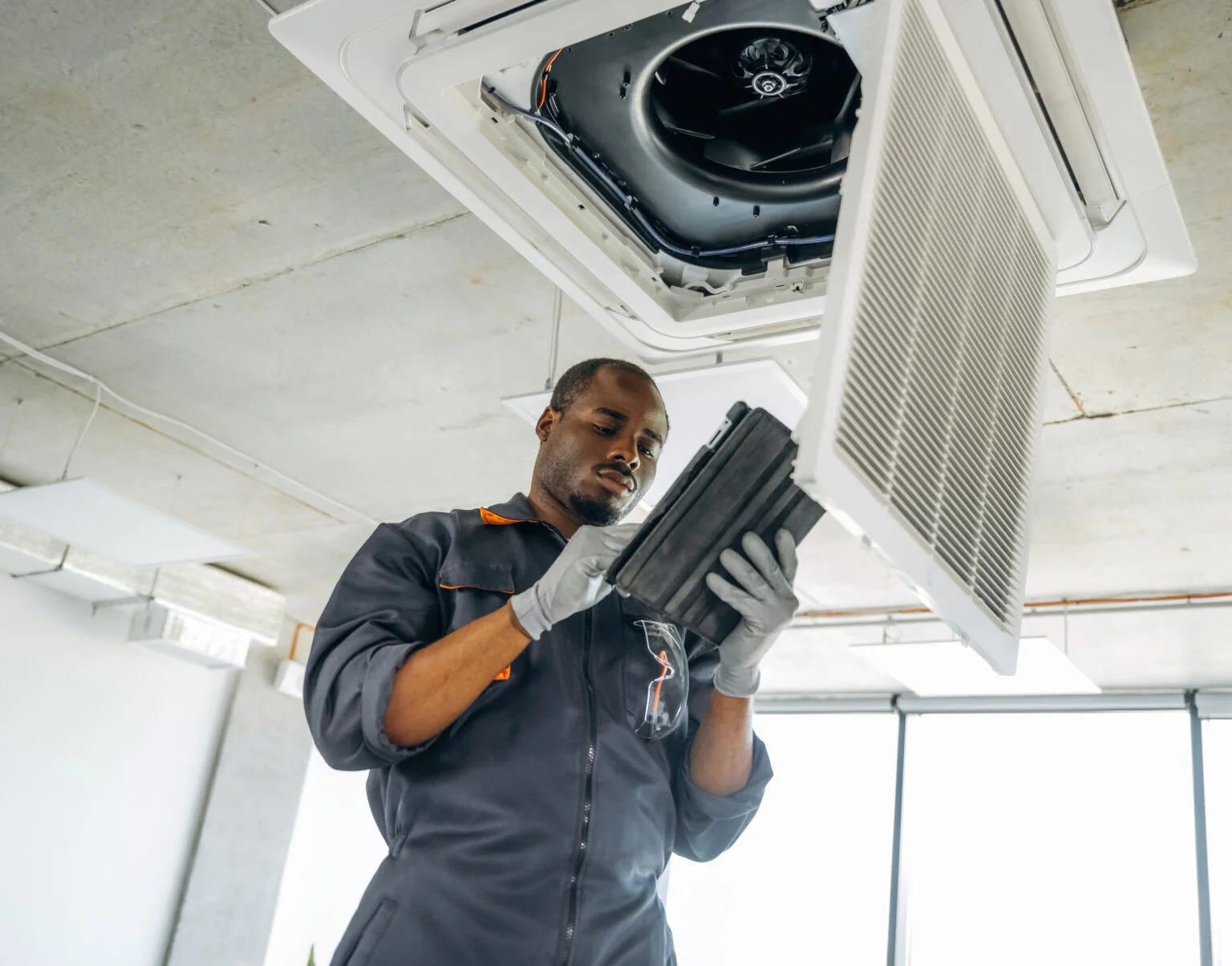 Technician inspecting a ceiling-mounted HVAC unit and its filter